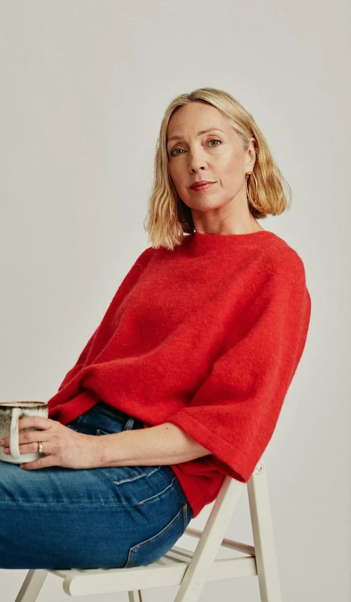 Alison, seated, holding a mug.