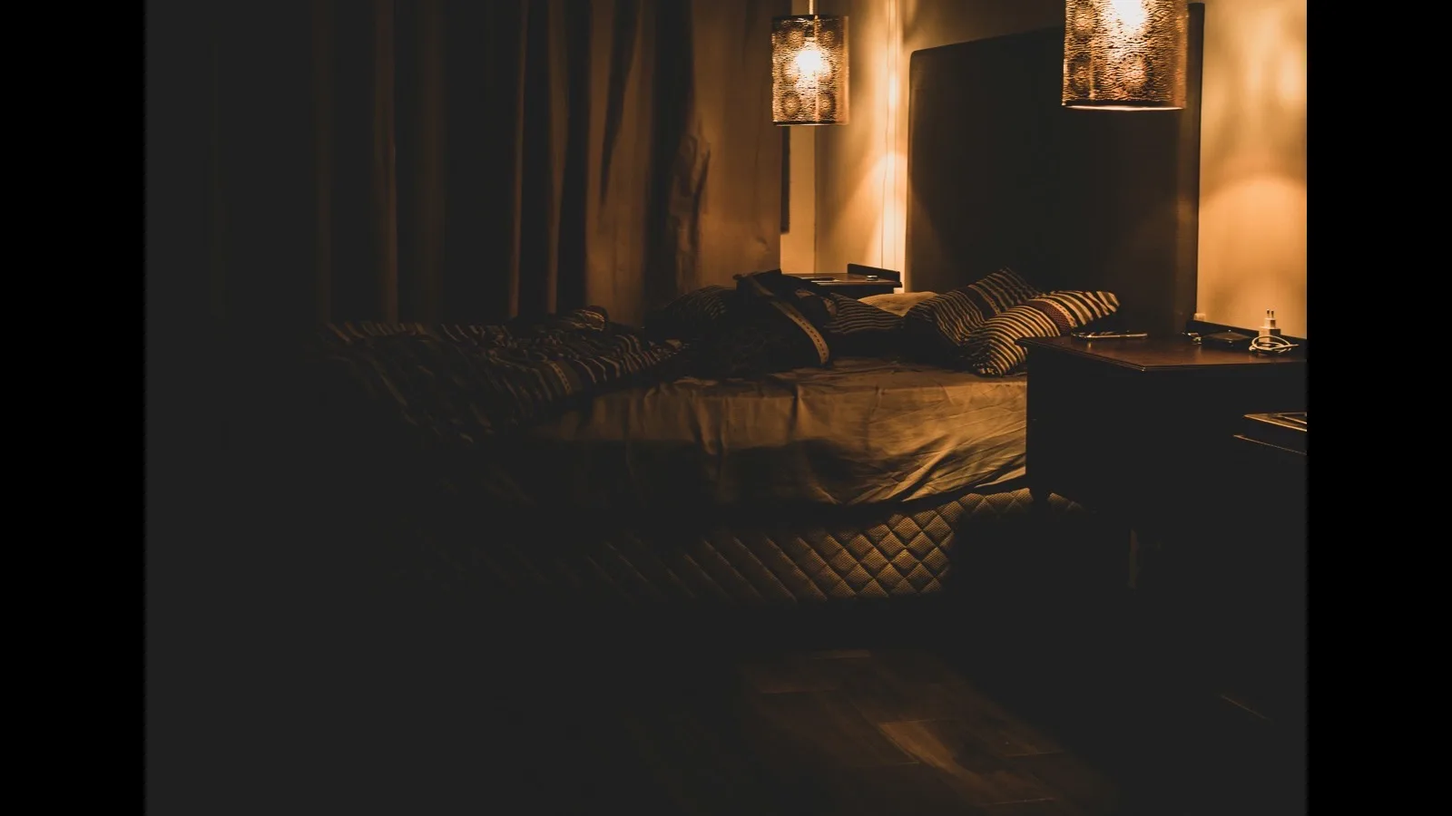 A dimly lit bedroom at night with two lamps glowing beside an unmade bed.