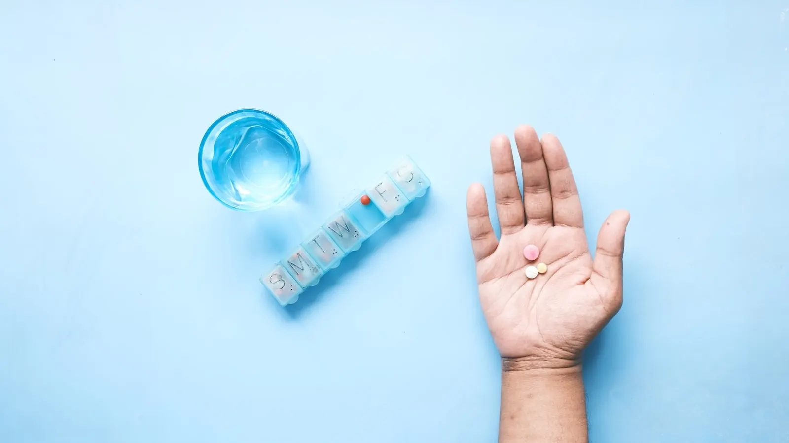 Pills in an open palm next to a glass of water.