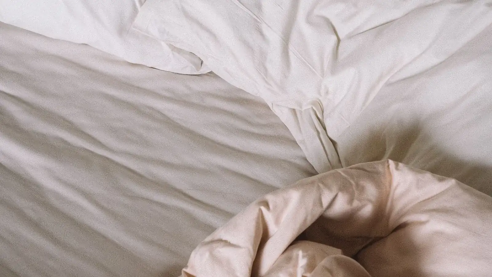 Rumpled white and blush bed linen photographed from above.