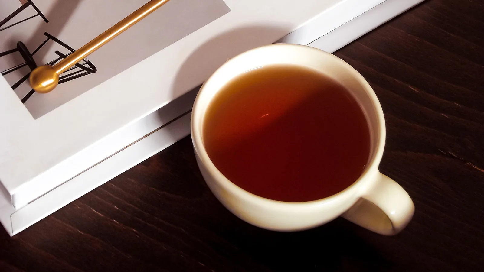 A cup of tea on a dark wooden table beside a stack of books in warm evening light.