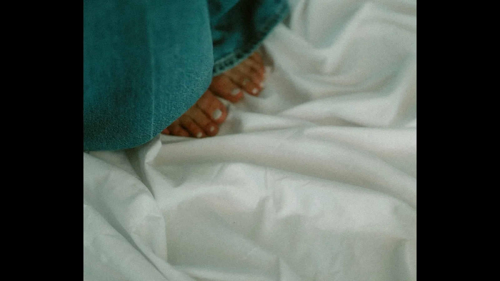 Bare feet resting on a rumpled white bed sheet.