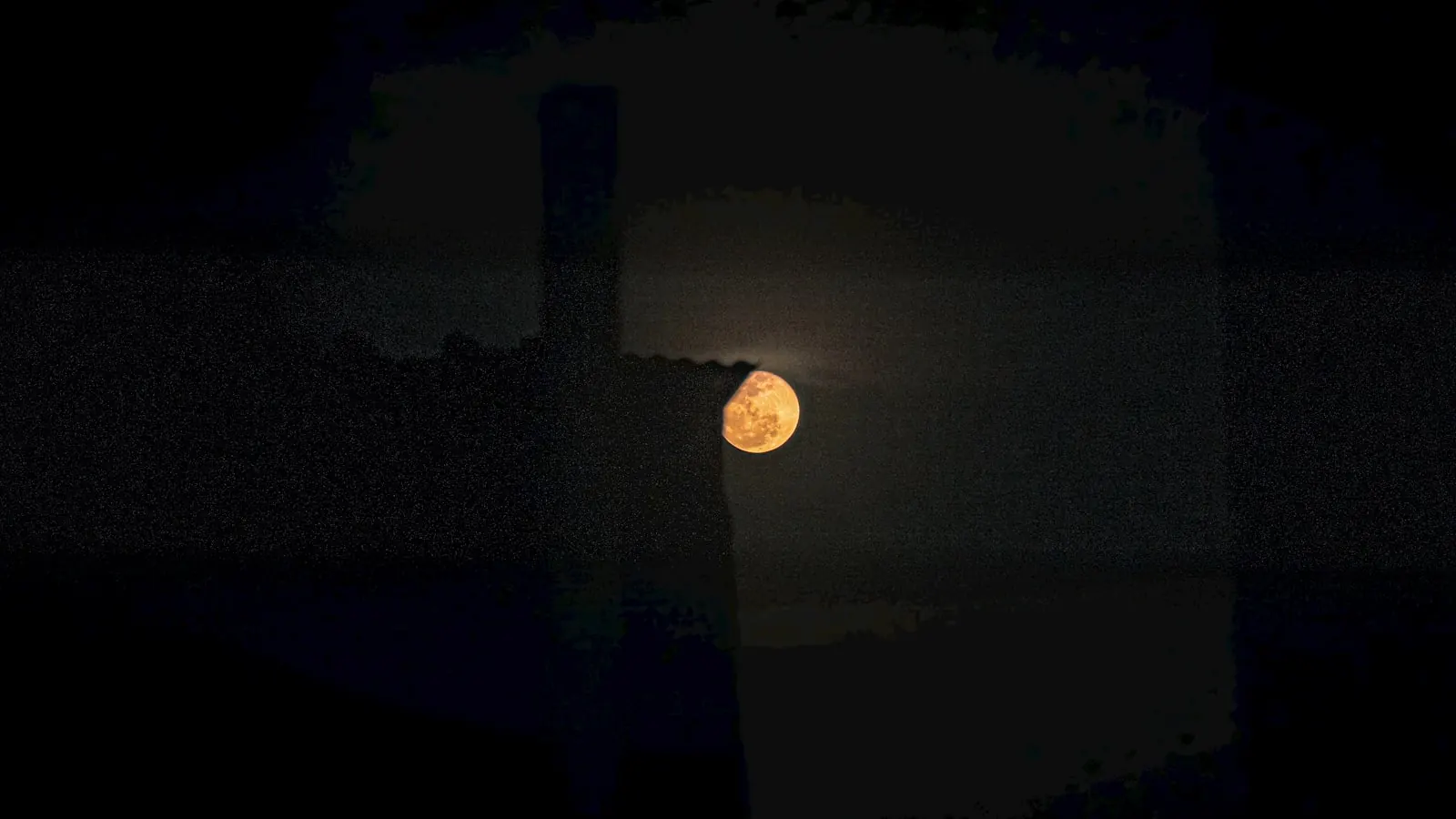 A full moon seen through a dark window at night.