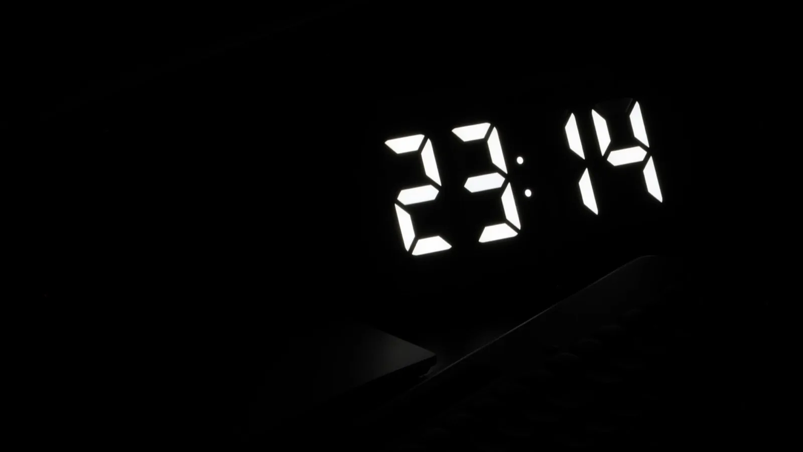 A digital clock glowing in the dark, displaying the time at night.